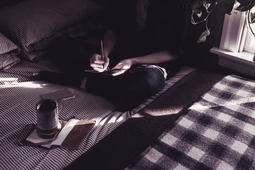 Persona escribiendo en una libreta junto a una ventana con luz cálida